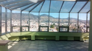 Quarto com uma grande janela que oferece vista para a paisagem urbana e montanhas.