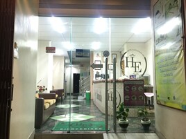 Uma área de recepção de hotel com um balcão, uma placa indicando 'Descuento' (Desconto) e um tapete de boas-vindas com a inscrição 'Bienvenidos' (Bem-vindos).