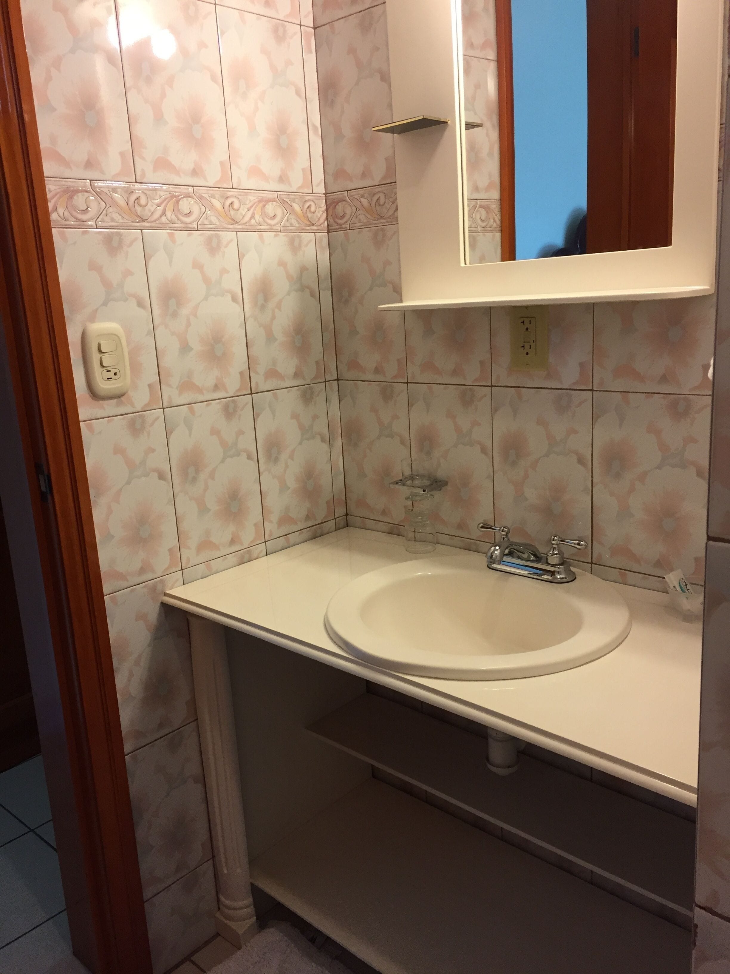 A bathroom with a white sink, a mirror above it, and floral patterned tiles on the walls.