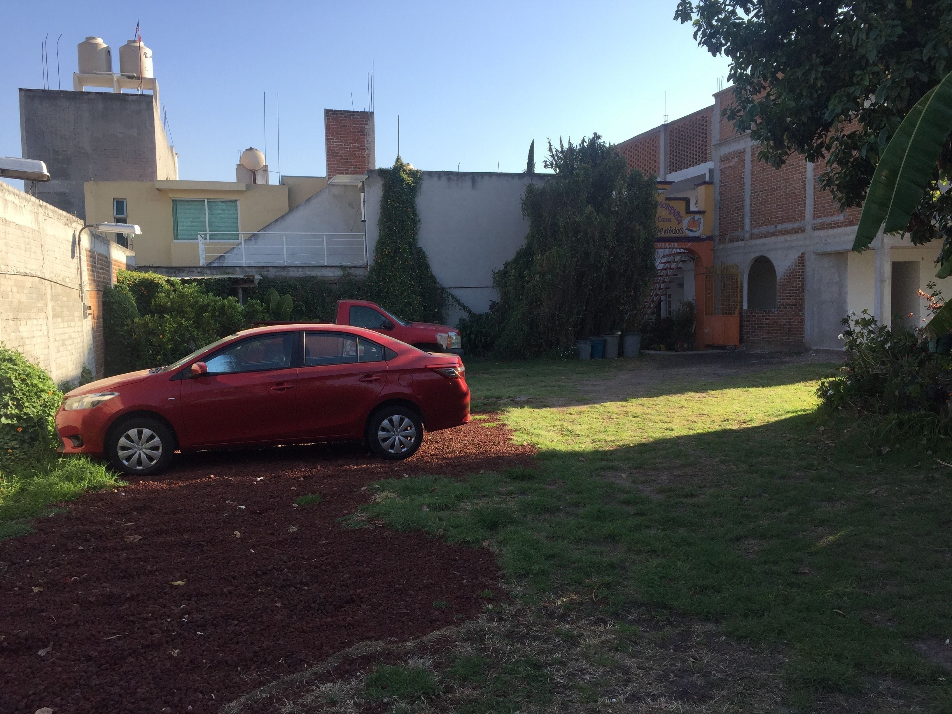 A red car parked in a driveway with a grassy yard and a brick building in the background.
