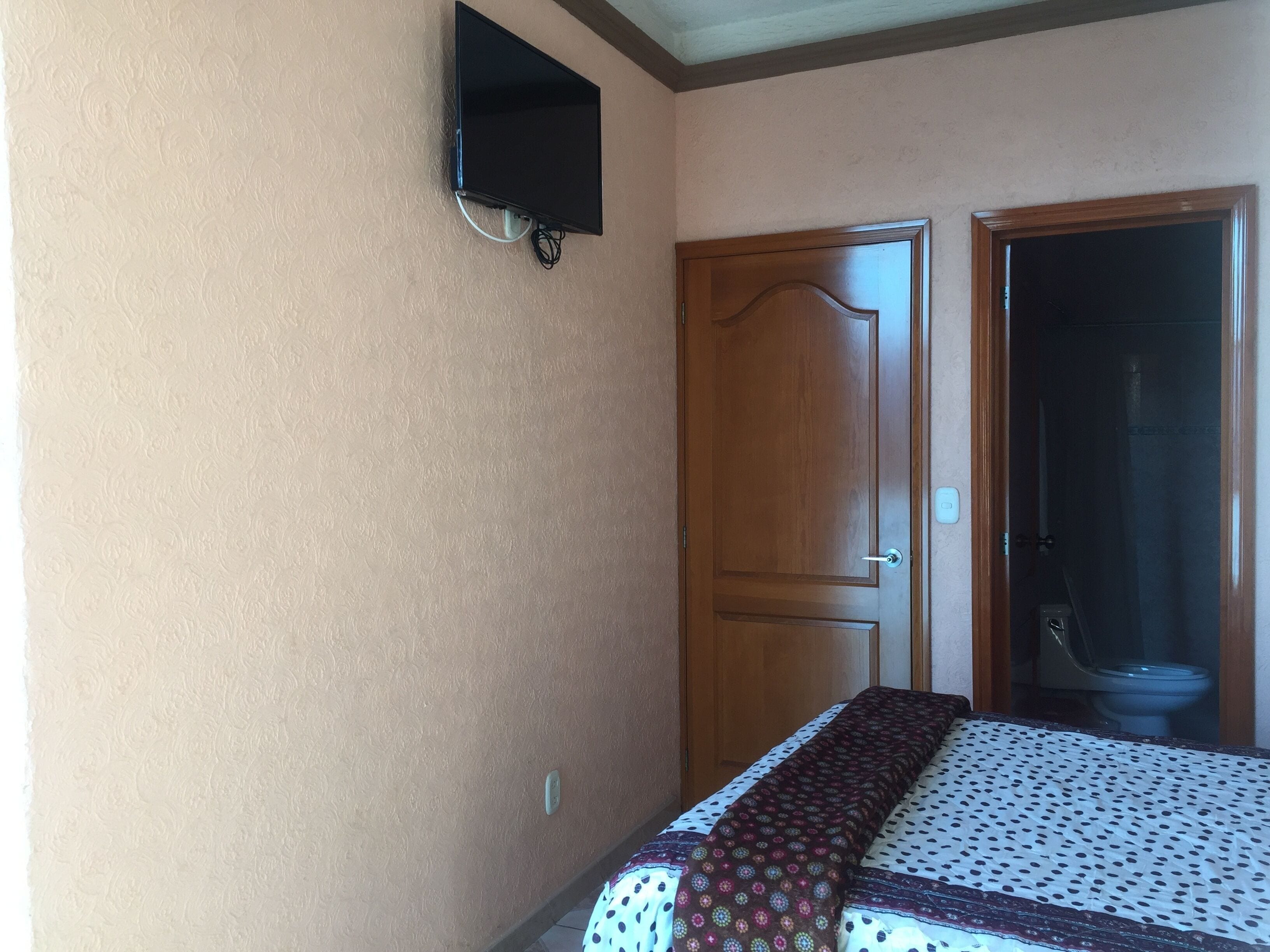 Un dormitorio con cama, una puerta de madera y televisor montado en la pared.