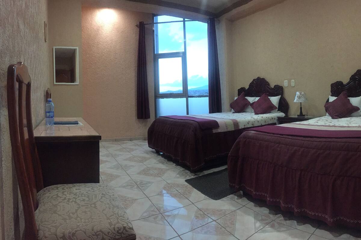 A hotel room with two beds, a desk, and a chair.
