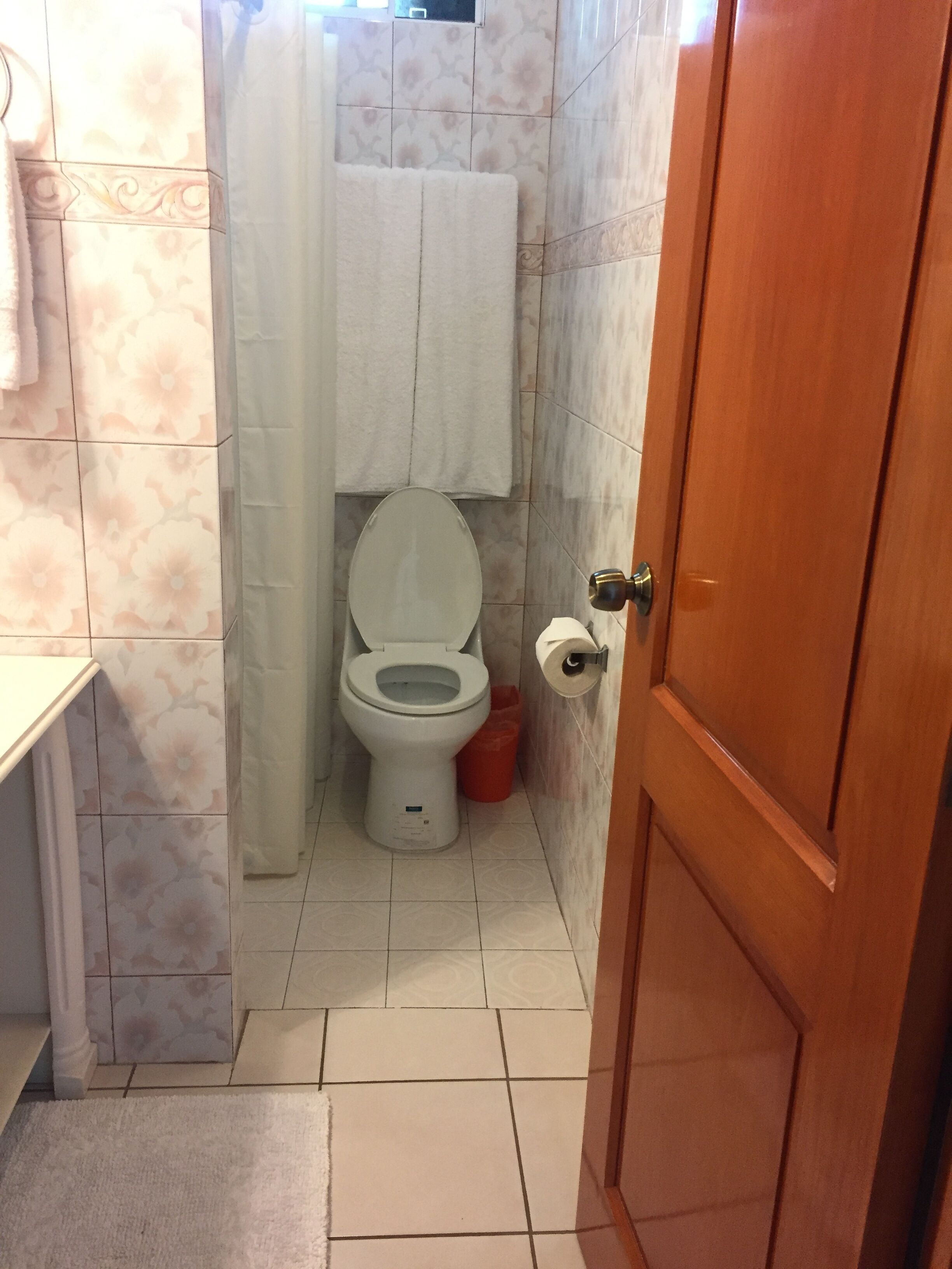 A small bathroom with a toilet, a roll of toilet paper, and a trash bin.