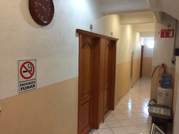 A hallway with a clock, a no-smoking sign, and a fire extinguisher. - Hotel Ejecutivo Inn (Ciudad Hidalgo)