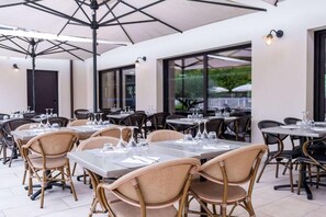 An outdoor dining area with tables and chairs, large umbrellas, and a view of the outdoors. - Brit Hotel Figeac (Figeac)