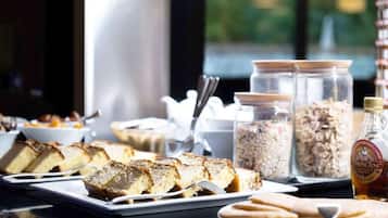 A breakfast buffet with sliced cakes, bowls of cereal, and jars of granola.