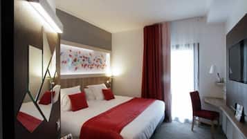 Habitació d'hotel amb un llit gran, escriptori amb cadira, televisió i finestra amb cortines.
