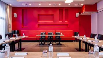 Un salón de conferencias con una pared decorada en rojo, varias mesas con sillas, botellas de agua y tarjetas de identificación.