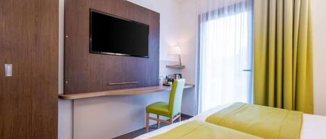 Habitación de hotel con cama, escritorio, silla, televisión y ventana con cortinas.