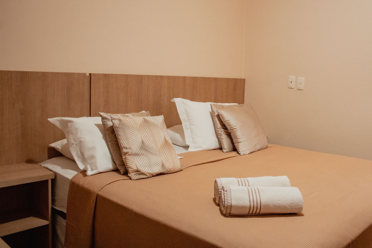 A neatly made bed with a brown bedspread and several pillows, including patterned and plain ones.