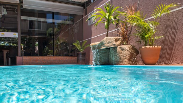 En swimmingpool med klart vand, omgivet af en murstensmur og krukker med planter.