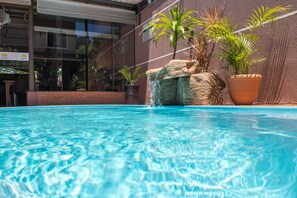 Una piscina de aguas claras, rodeada por un muro de ladrillo y plantas en macetas.