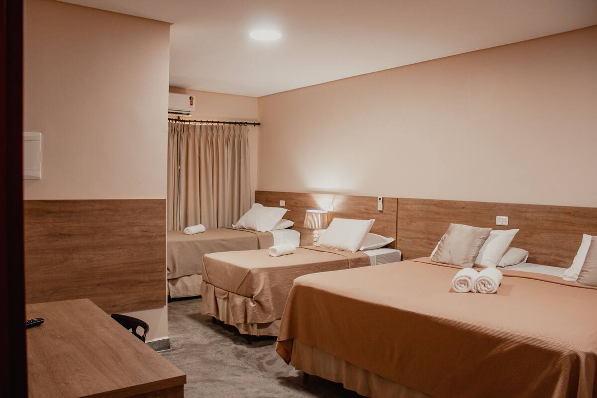A hotel room with two single beds, a wooden headboard, a desk, and a chair.