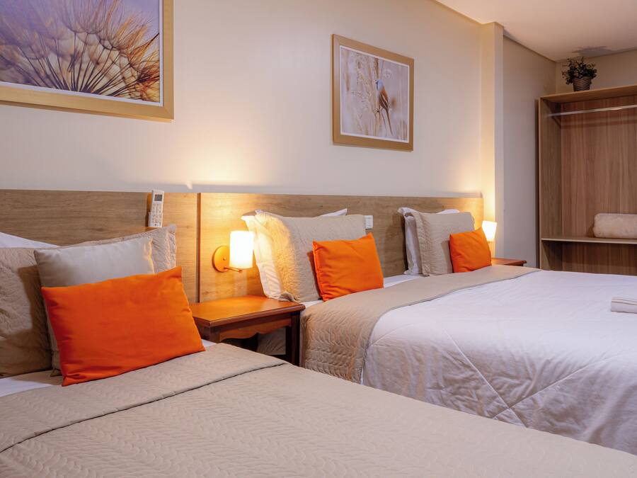 A hotel room with two beds, a wooden headboard, a nightstand with a lamp, and a wooden wardrobe.
