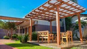 Et overdækket udendørs opholdsområde med træmøbler og et pergola-tag.