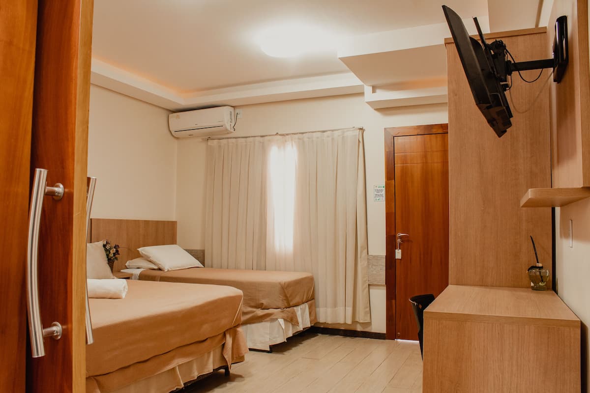 A hotel room with two beds, a TV mounted on the wall, a wooden cabinet, and a door with a sign.