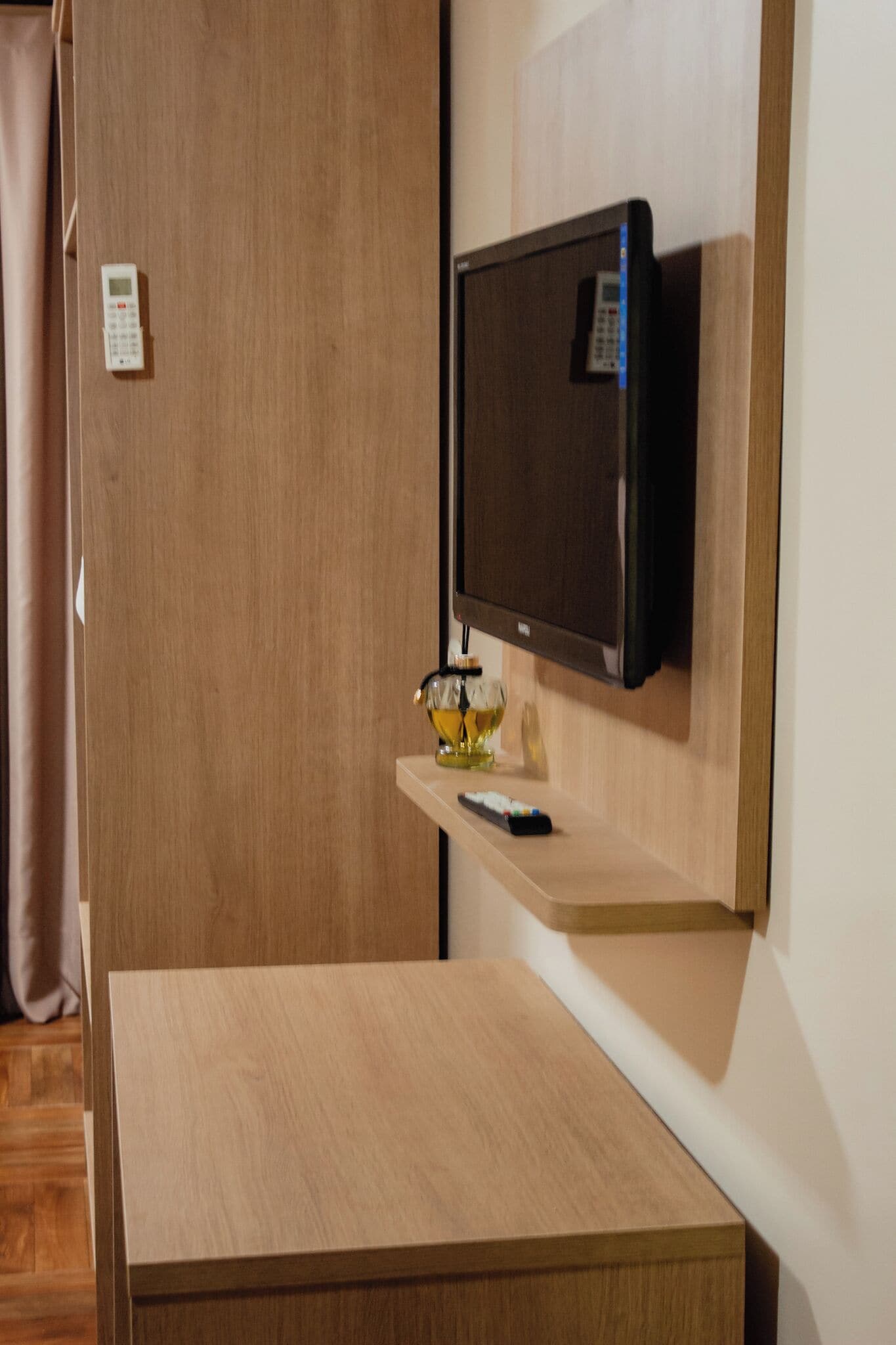 A hotel room with a wooden desk, a mounted television, and a remote control on the desk.