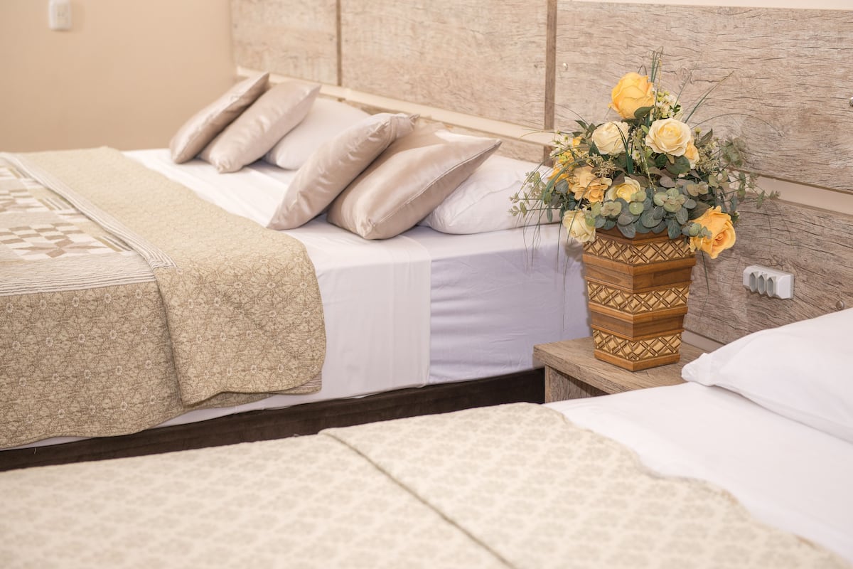 A hotel room with a bed, pillows, a bedside table with a vase of flowers, and a headboard.
