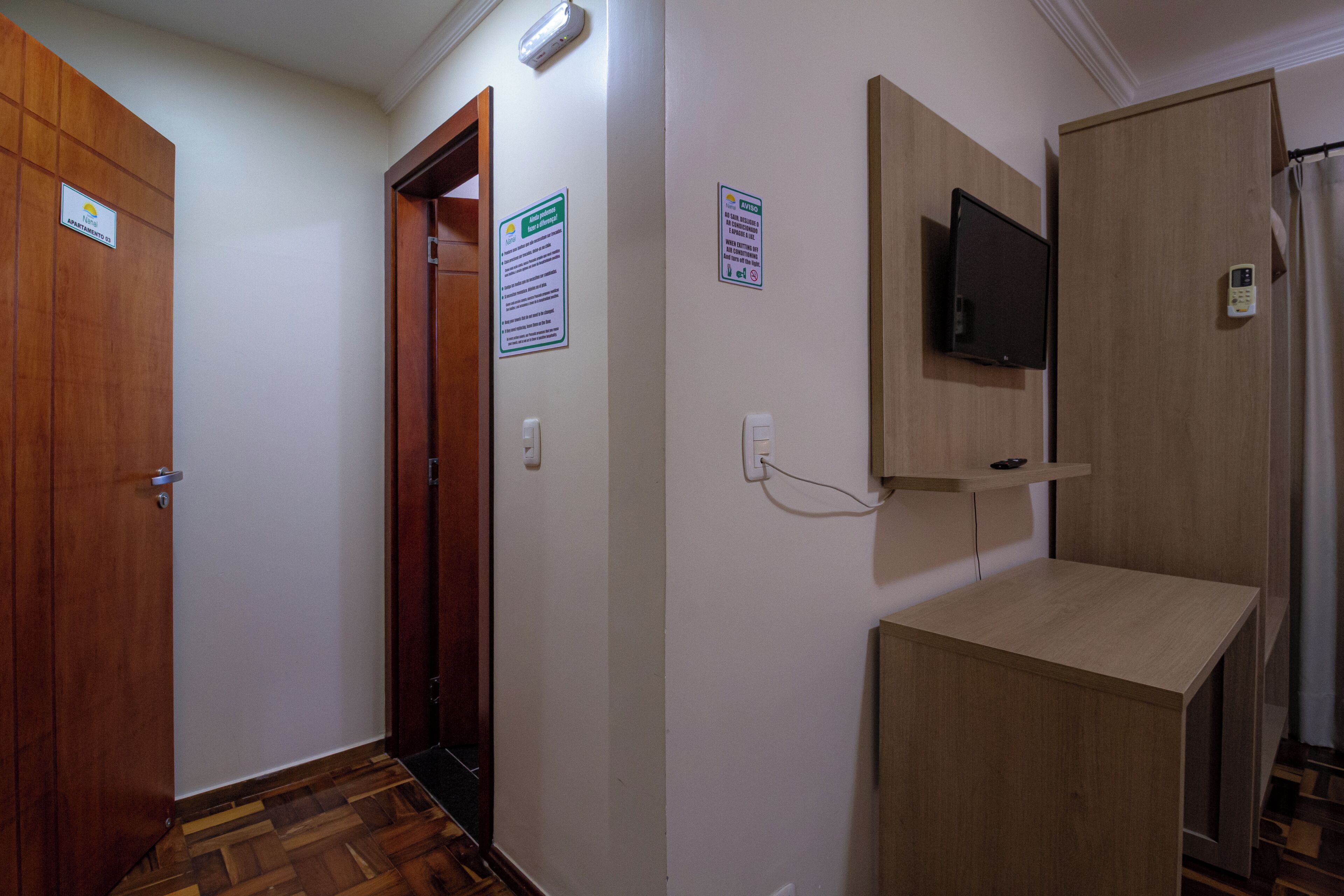 Un passadís amb portes de fusta, un televisor penjat i un petit armari de fusta.