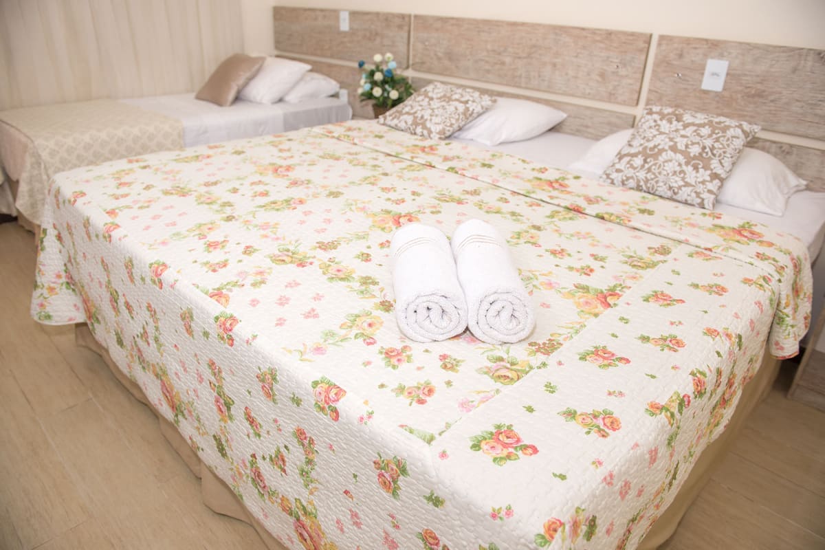 A hotel room with a large bed, two smaller beds, and a nightstand with a vase of flowers.