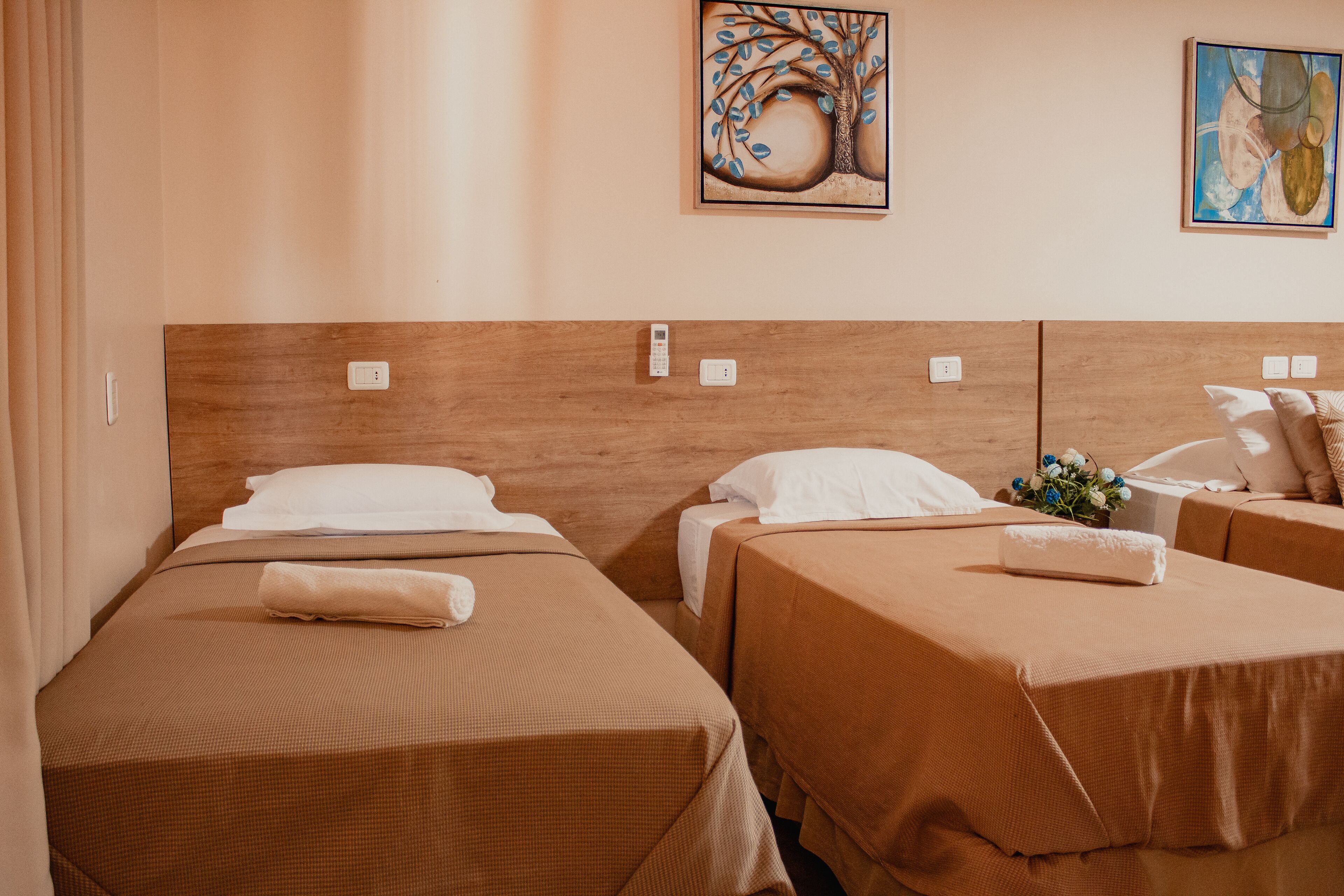 Quarto de hotel com duas camas de solteiro, cada uma com cabeceira de madeira, roupa de cama branca e uma pequena mesa de cabeceira com abajur.