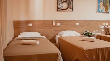 Quarto de hotel com duas camas de solteiro, cada uma com cabeceira de madeira, roupa de cama branca e uma pequena mesa de cabeceira com abajur.