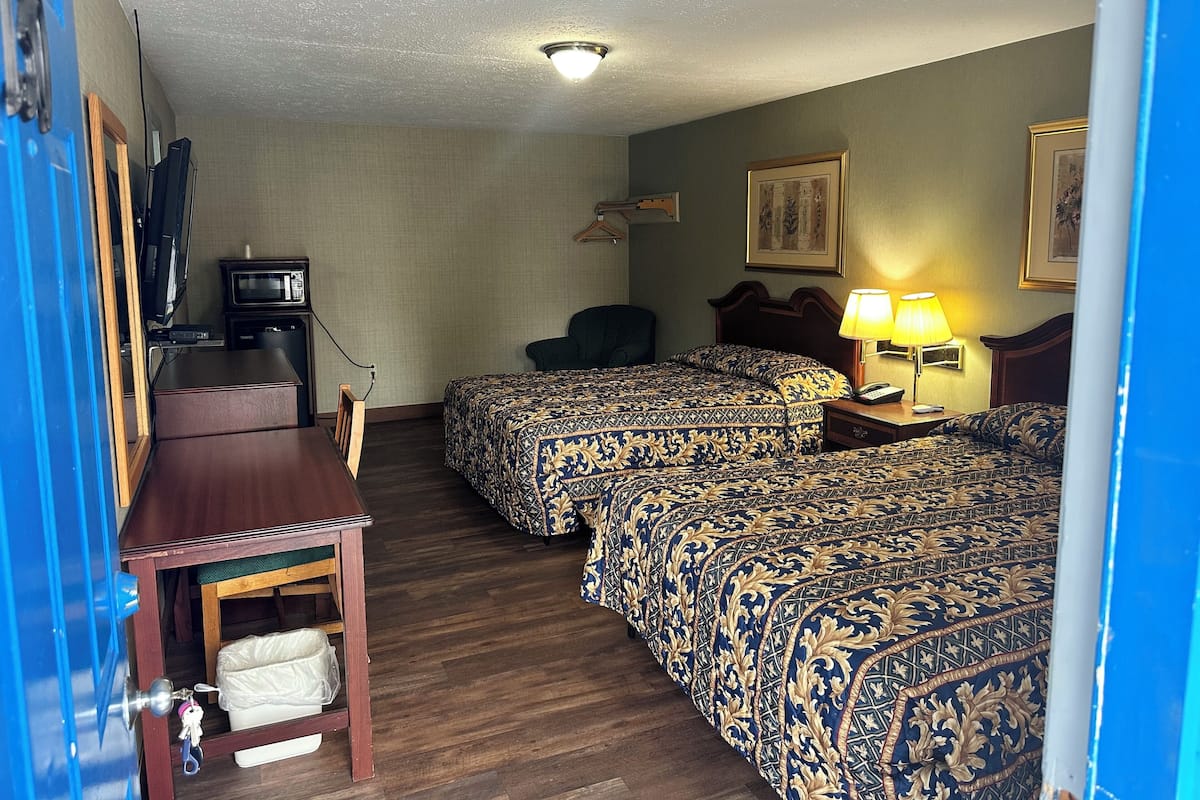 A hotel room with two beds, a desk with a chair, a television, a microwave, and a lamp.