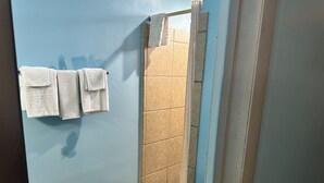 A bathroom with a blue wall, a shower area with beige tiles, and three white towels hanging on the wall. - Westgate Manor Motel Austintown-Younstown, Ohio (Austintown)