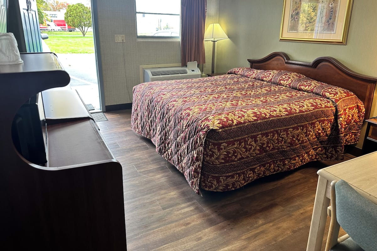 A hotel room with a bed, a desk, a chair, a lamp, and a window with curtains.