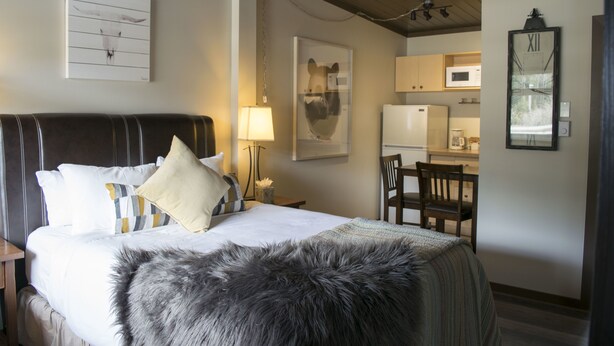 A hotel room with a large bed, a desk with a chair, a microwave, and a kitchen area. - Yamnuska Suites (Dead Man's Flats)