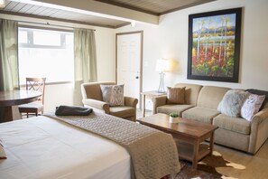 Habitación de hotel con cama, dos sofás, una mesa de centro, lámpara, un cuadro y vistas al exterior.
