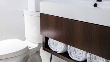 A modern bathroom with a white toilet, a white sink with a black faucet, a hanging plant, and a towel rack with white towels.