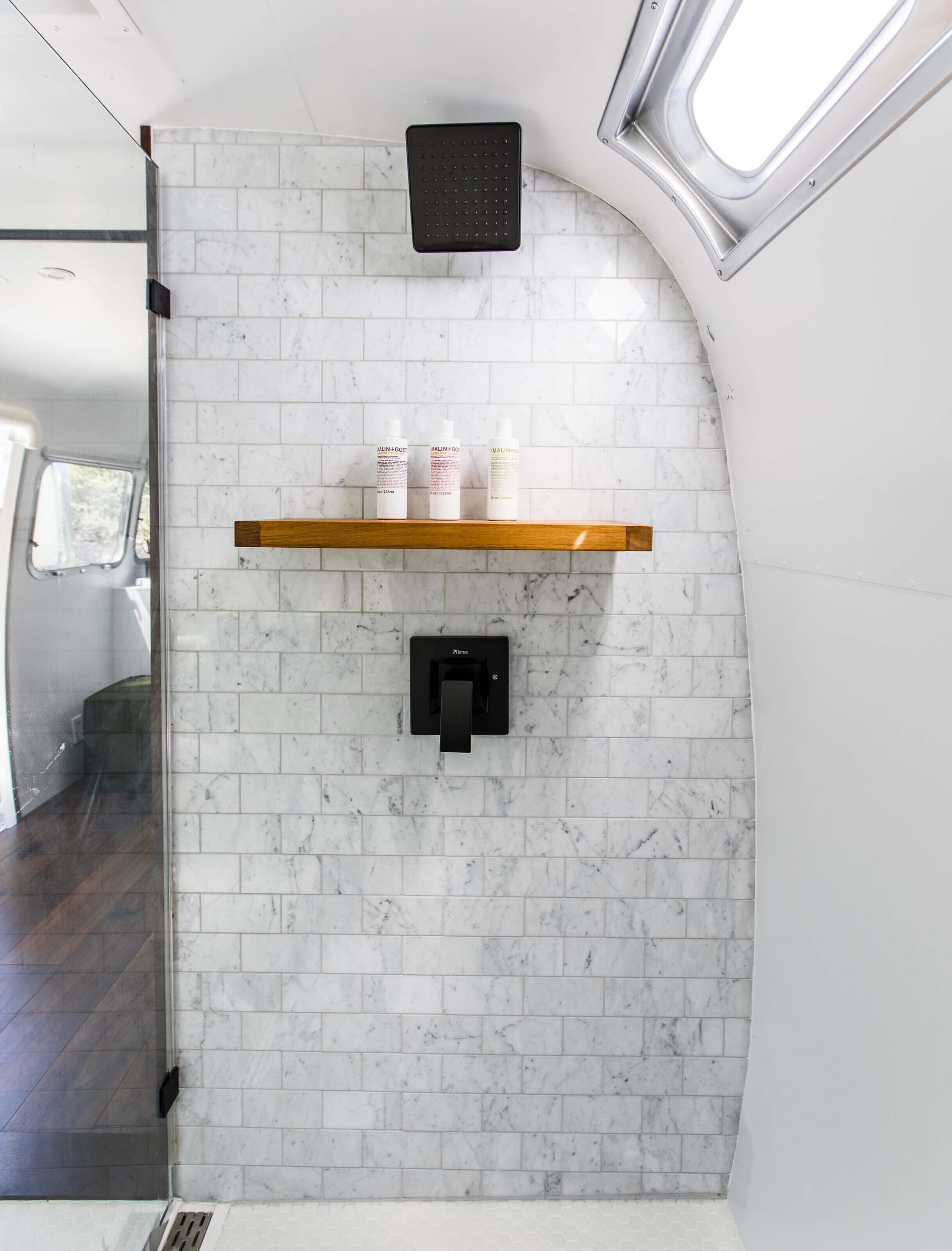 A bathroom with white marble tiles, a black faucet, and a shelf with three bottles.