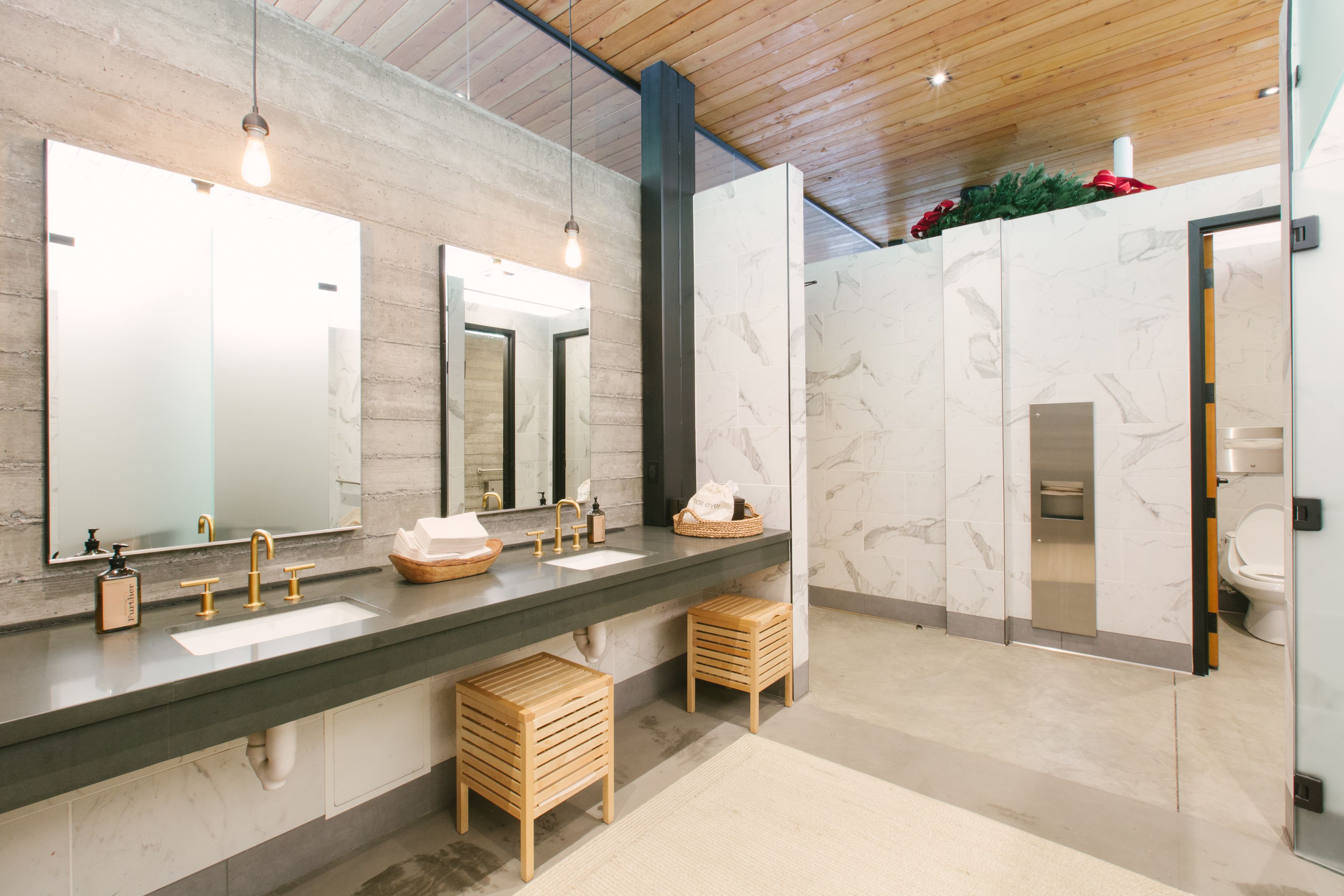 A modern bathroom with two sinks, wooden stools, and a large mirror.