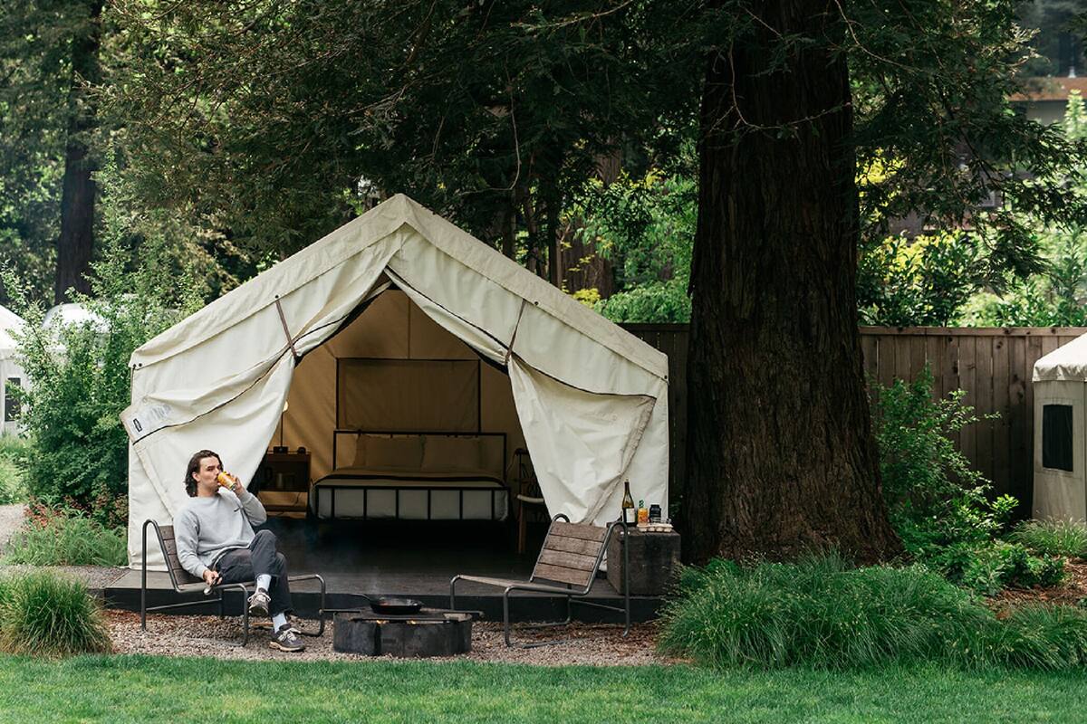 A tented accommodation with a bench and a table, surrounded by greenery and trees.