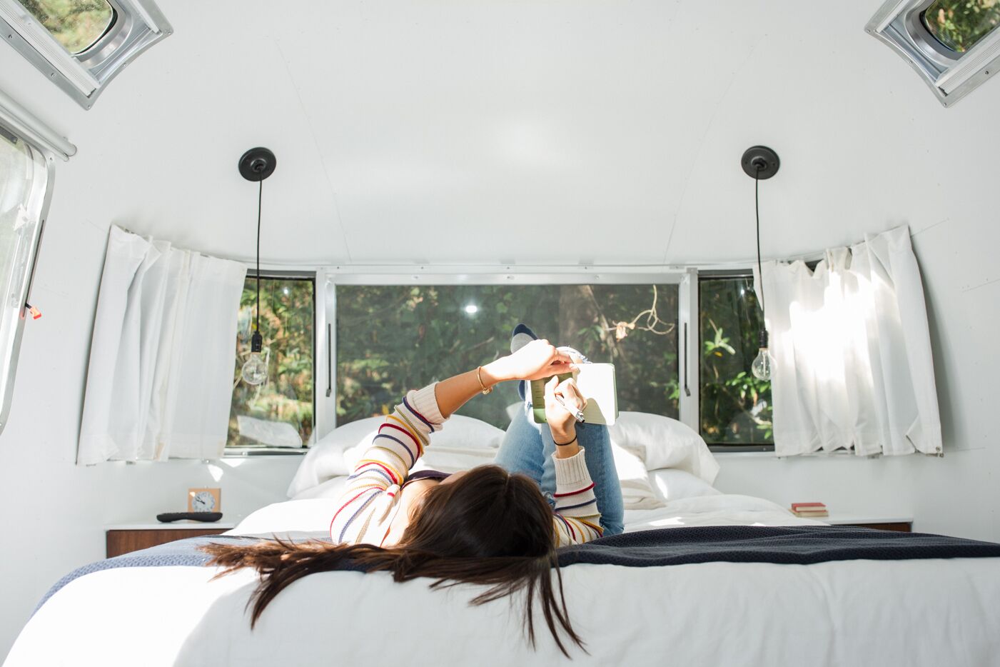 Un dormitorio con un ventanal grande, una cama y una mesita de noche con lámpara.