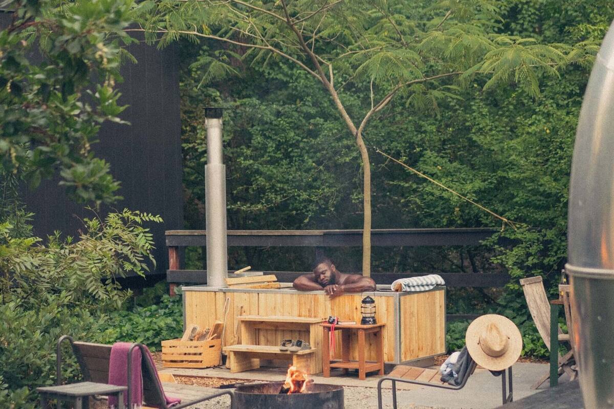 A rustic outdoor seating area with a fire pit, wooden benches, and a large metal container.