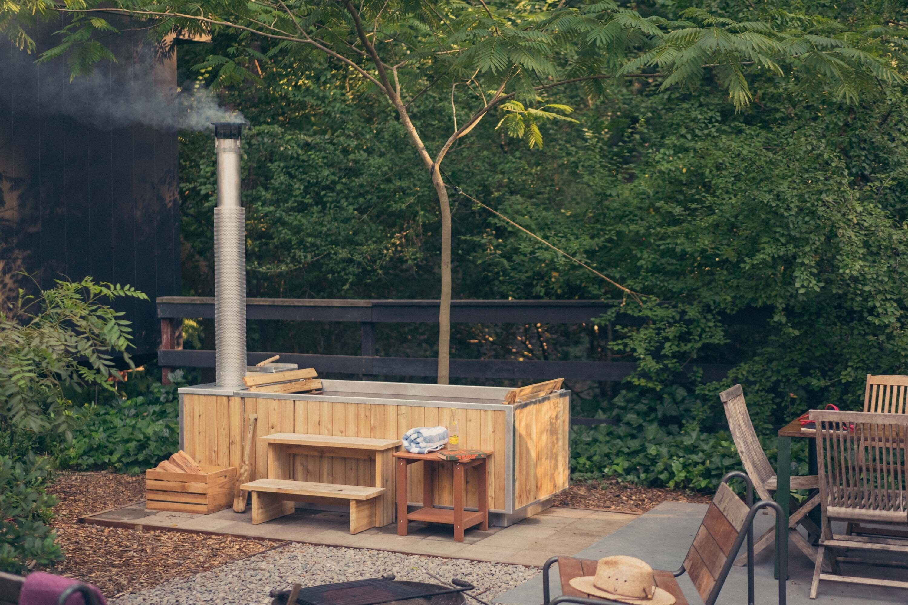 A wooden outdoor seating area with a hot tub, benches, and a grill.