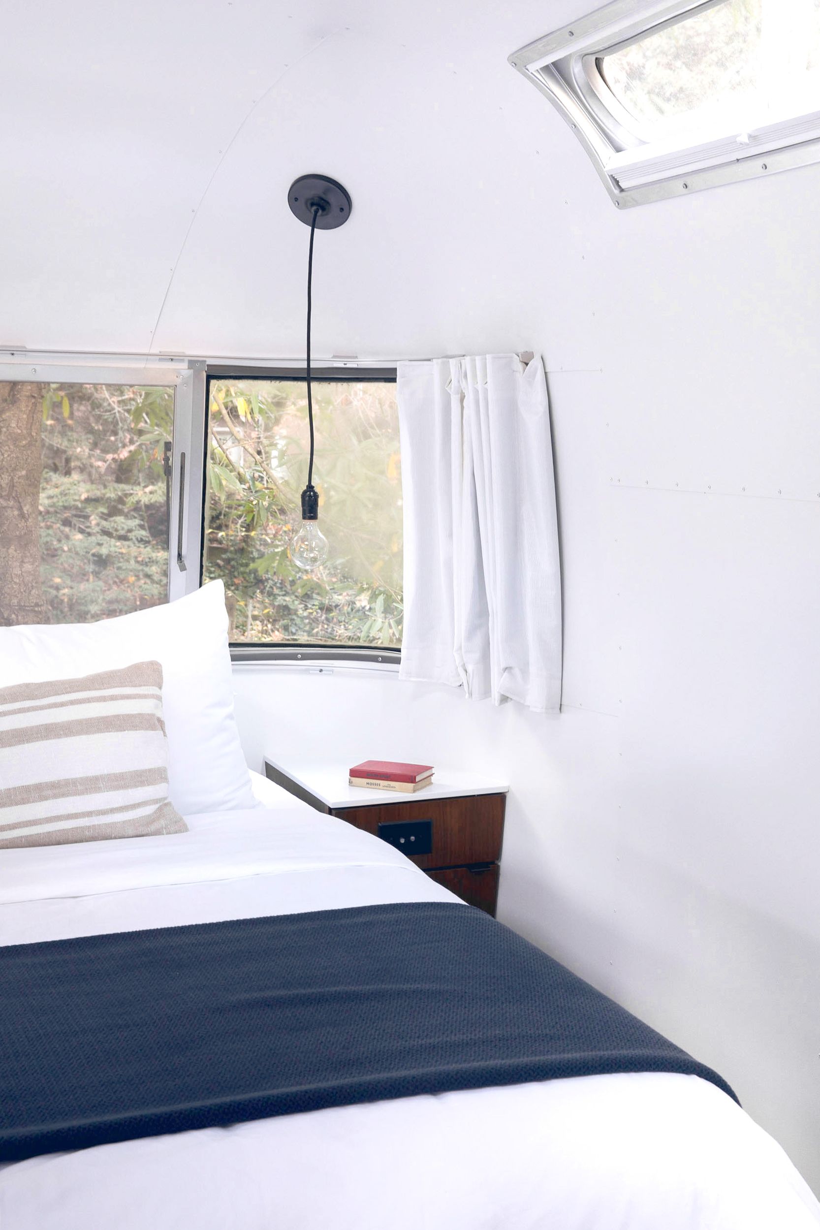 A bedroom with a bed, a bedside table, a window with curtains, and a skylight.