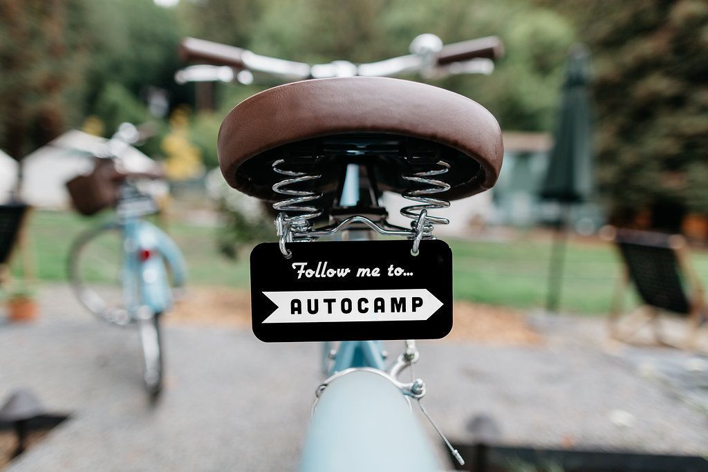A bicycle with a sign attached to the handlebars that reads "Follow me to... AUTOCAMP".