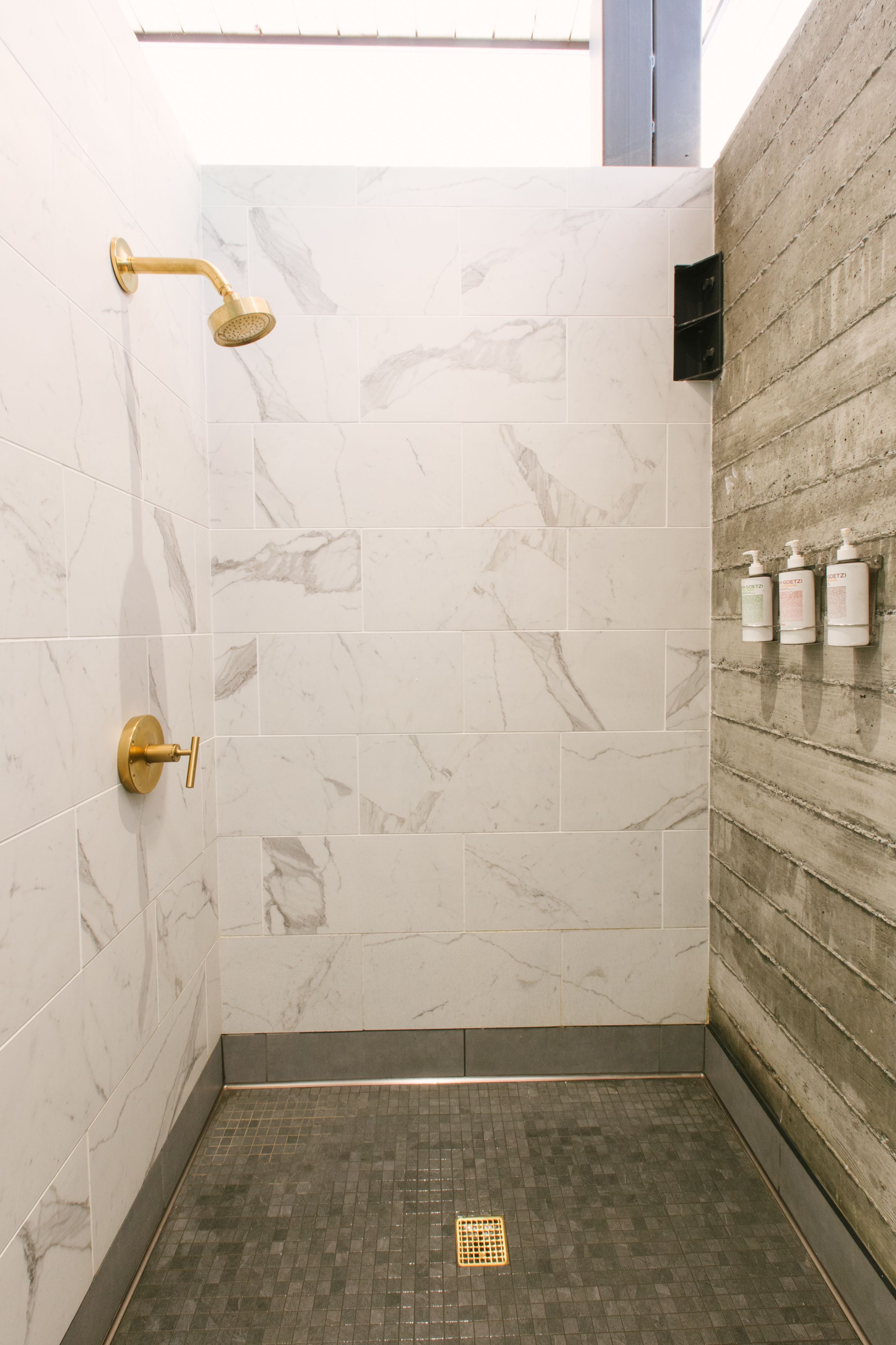 Une douche dotée d’un pommeau de douche doré et d’un mur recouvert de carreaux de marbre.