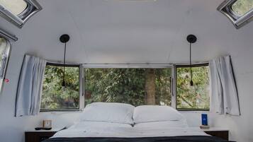 A bedroom with a large bed, two windows, a bedside table with a book, and a clock.