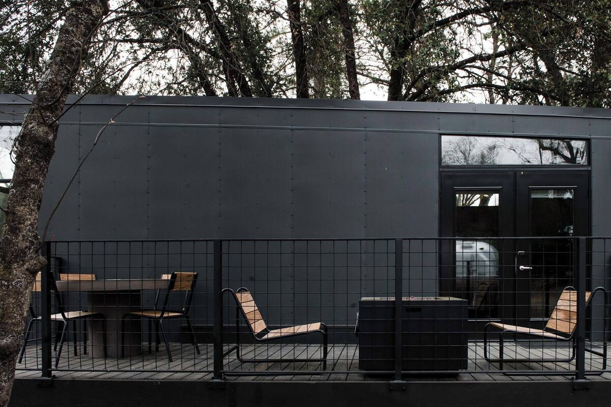 A modern building with a dark exterior, a glass door entrance, and outdoor seating with metal chairs and a table.