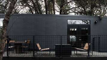 A modern building with a dark exterior, a glass door entrance, and outdoor seating with metal chairs and a table.