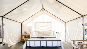 A tented room with a bed, a small table, and a chair. - AutoCamp Sonoma (Guerneville)