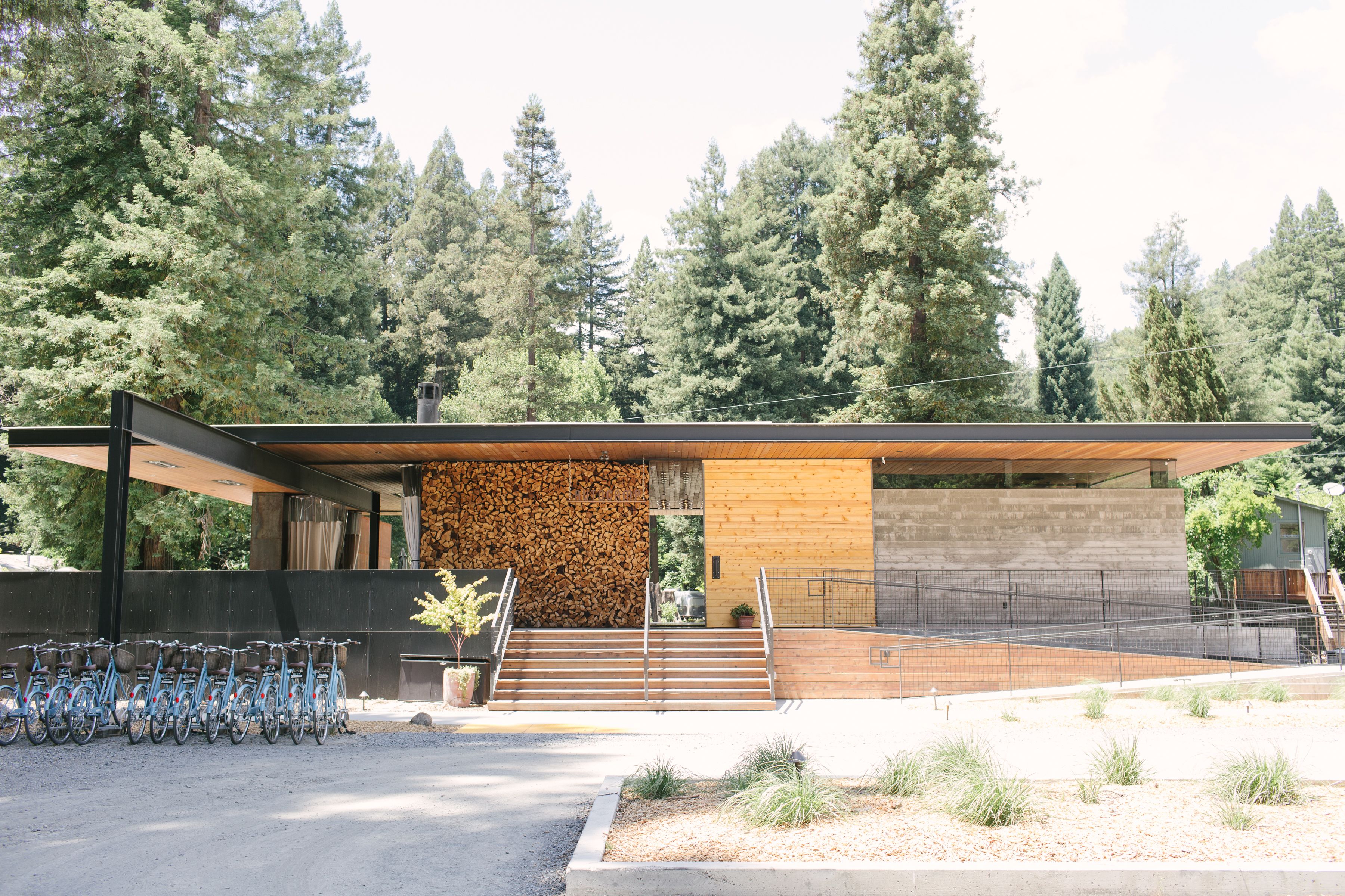 A modern building with a wooden facade, a staircase leading to a covered entrance, and a row of bicycles parked outside.