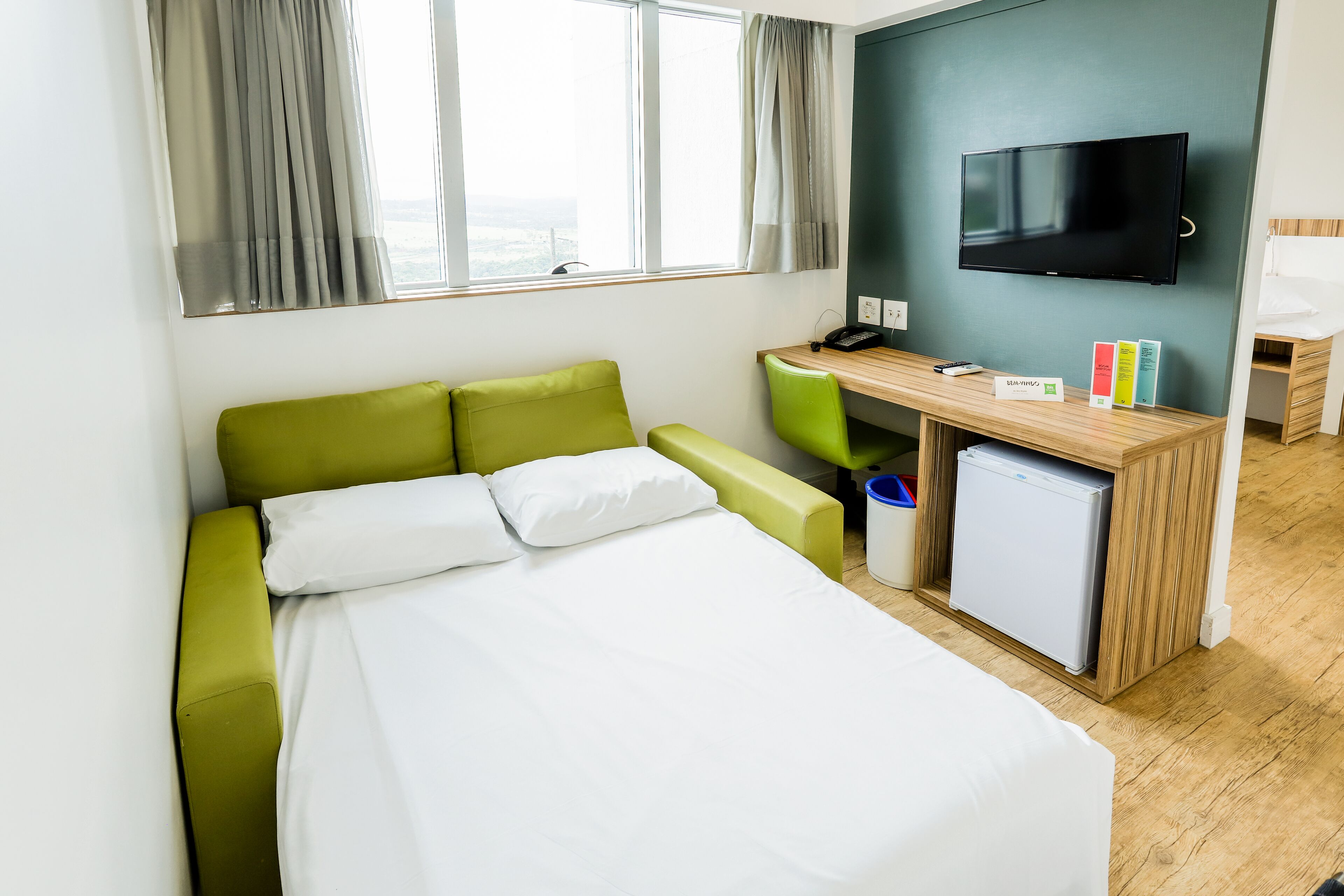 A hotel room with a bed, a desk, a television, and a small refrigerator.