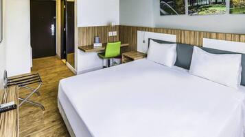 Ett hotellrum med en stor säng, ett skrivbord med en stol, en spegel och utsikt över en golfbana genom fönstret.