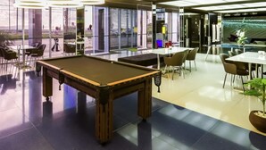 Un área moderna con mesa de billar en el interior, con mesa de billar, asientos y un gran ventanal con vistas al exterior.