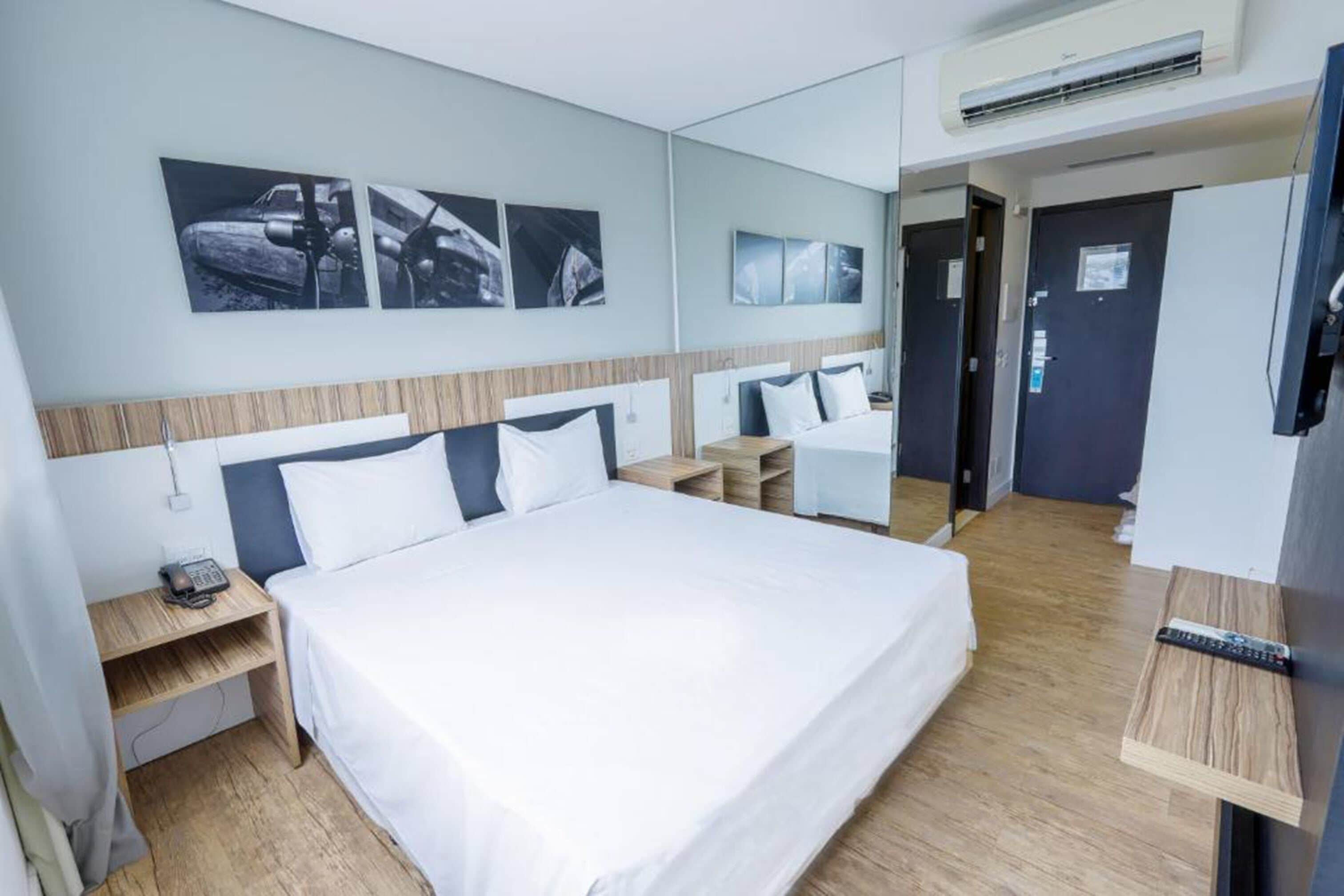 Quarto de hotel com uma cama grande, mesas de cabeceira, escrivaninha e televisão.